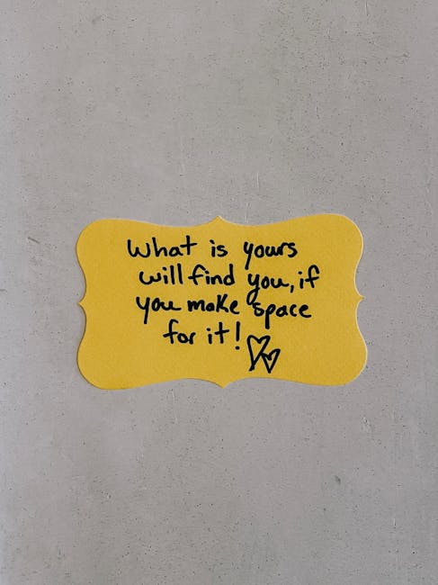 A close-up image of a bright yellow, scalloped-edged sticky note attached to a plain, light-colored wall. The note contains handwritten black ink text that reads: